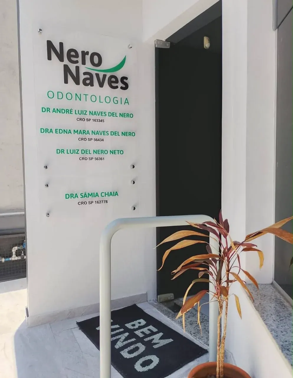A entrada do consultório, com a placa dos dentistas ao lado da porta e o capacho de bem-vindo.